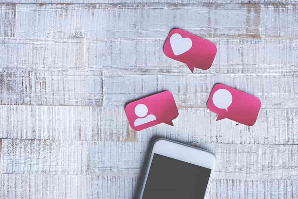 Smartphone auf Tisch mit Herz, Profil und Chat-Icon